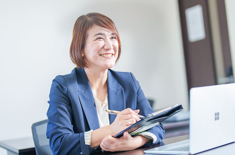 小日向香緒里さんが笑顔で相手の方と話をしながらクリップボードに書き込みをしている写真